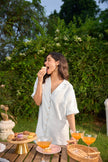 Woman enjoying a snack outdoors with a table of food and drinks in the background