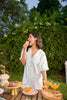 Woman enjoying a snack outdoors with a table of food and drinks in the background