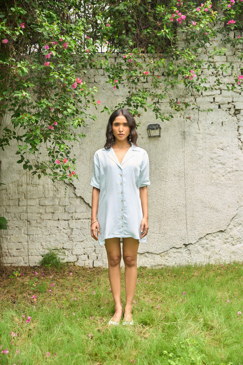 Woman standing in a garden with a white brick wall and greenery in the background
