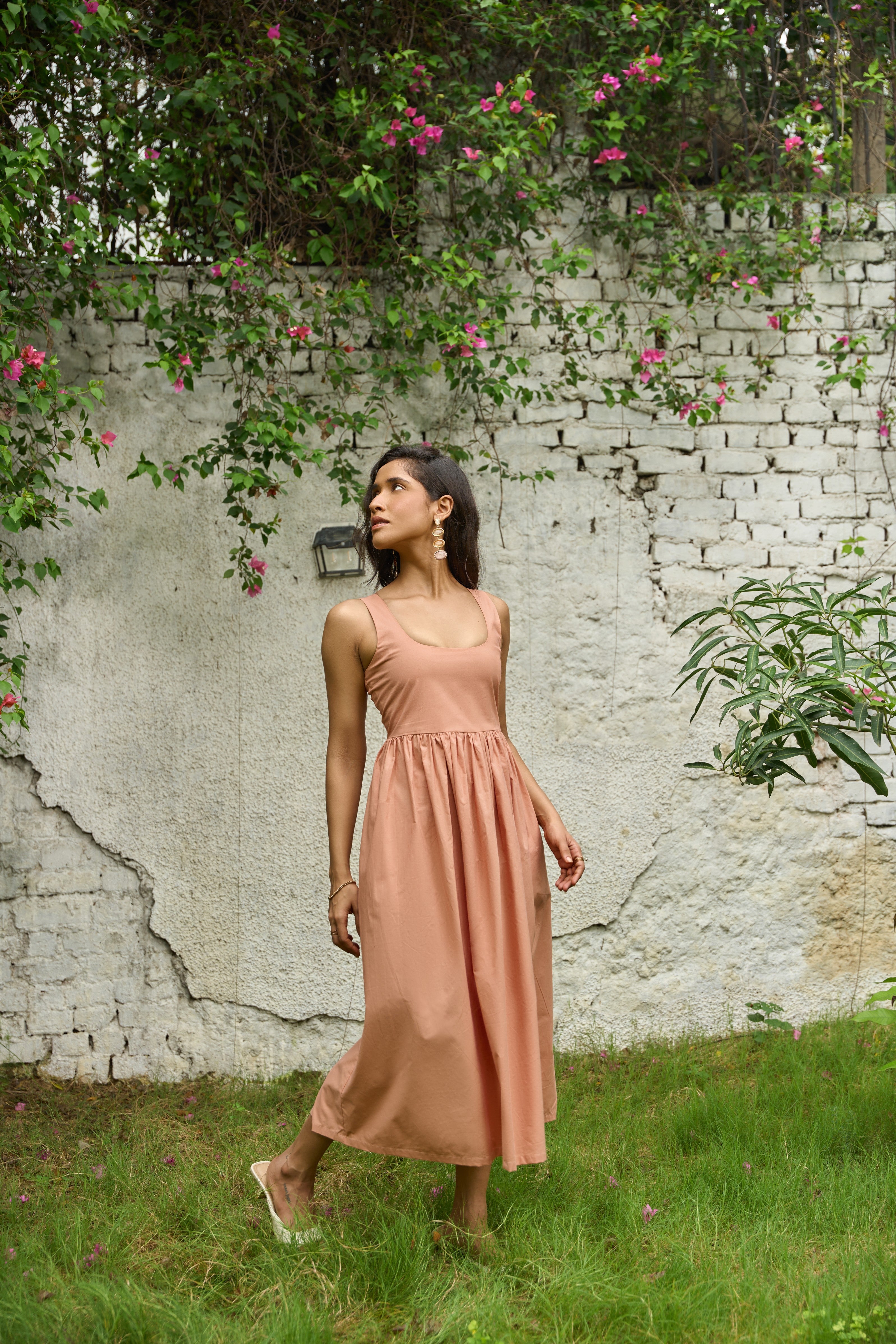Woman in a pink dress standing in front of a textured wall with greenery