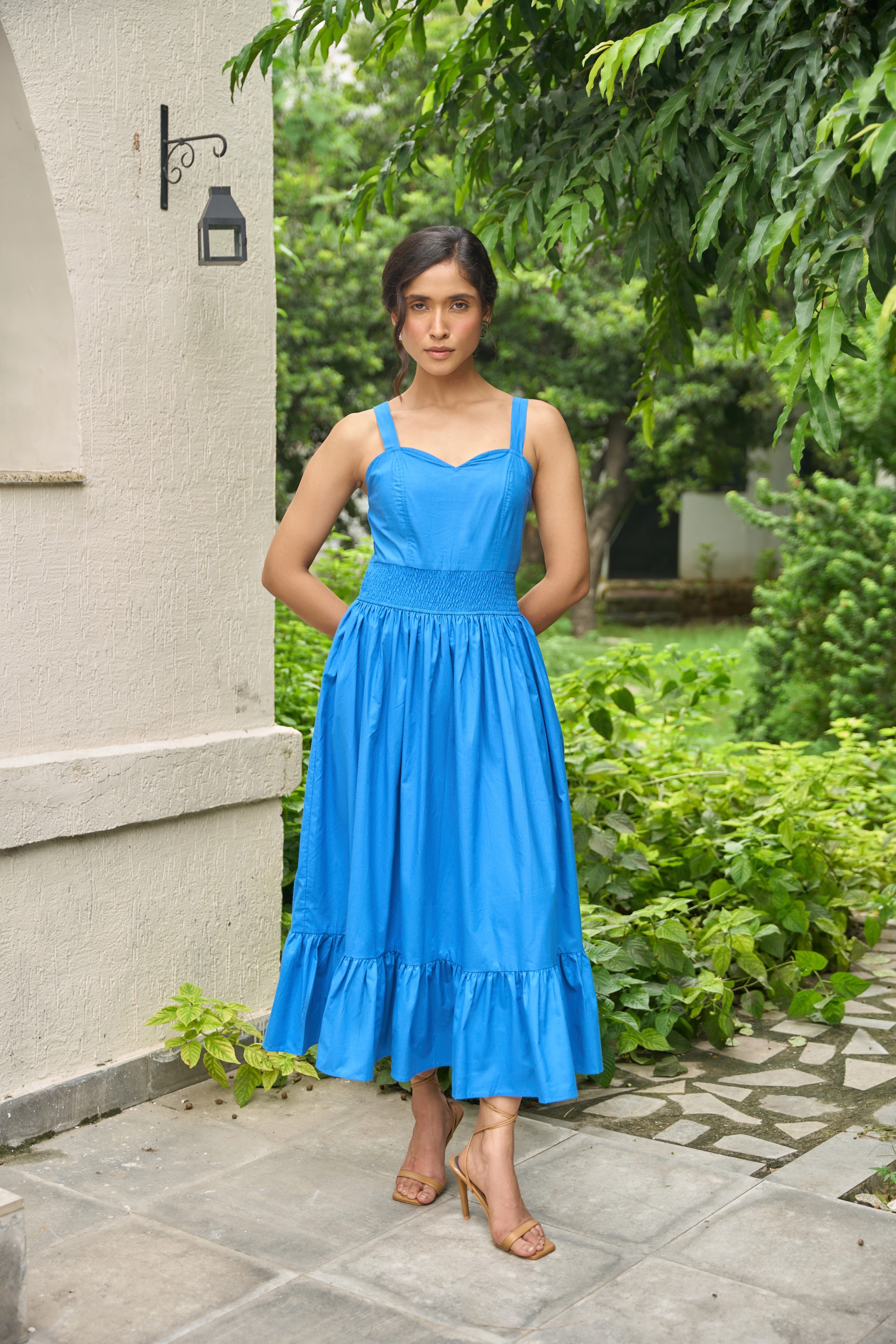Woman in a blue dress standing outdoors near a stone wall and greenery