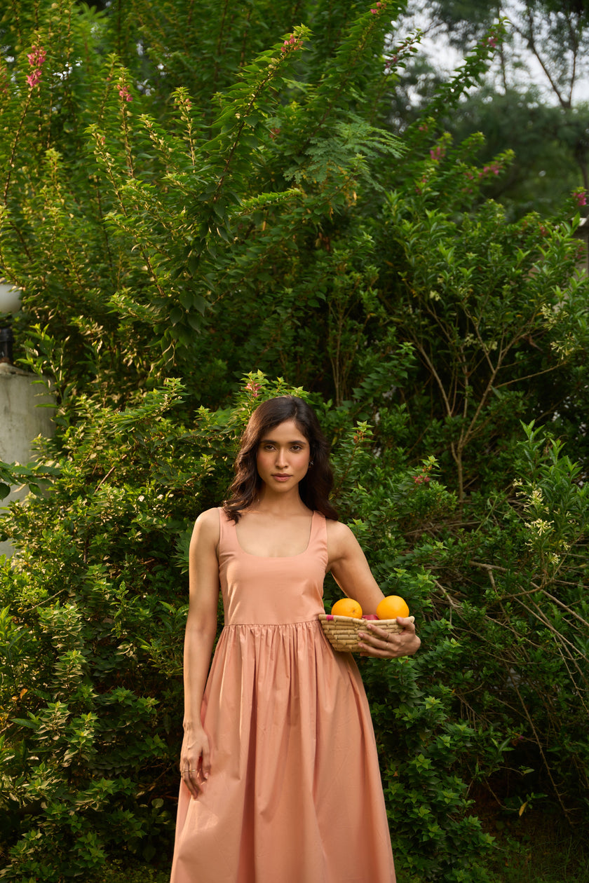 Woman in a peach dress holding a basket of oranges in a green outdoor setting