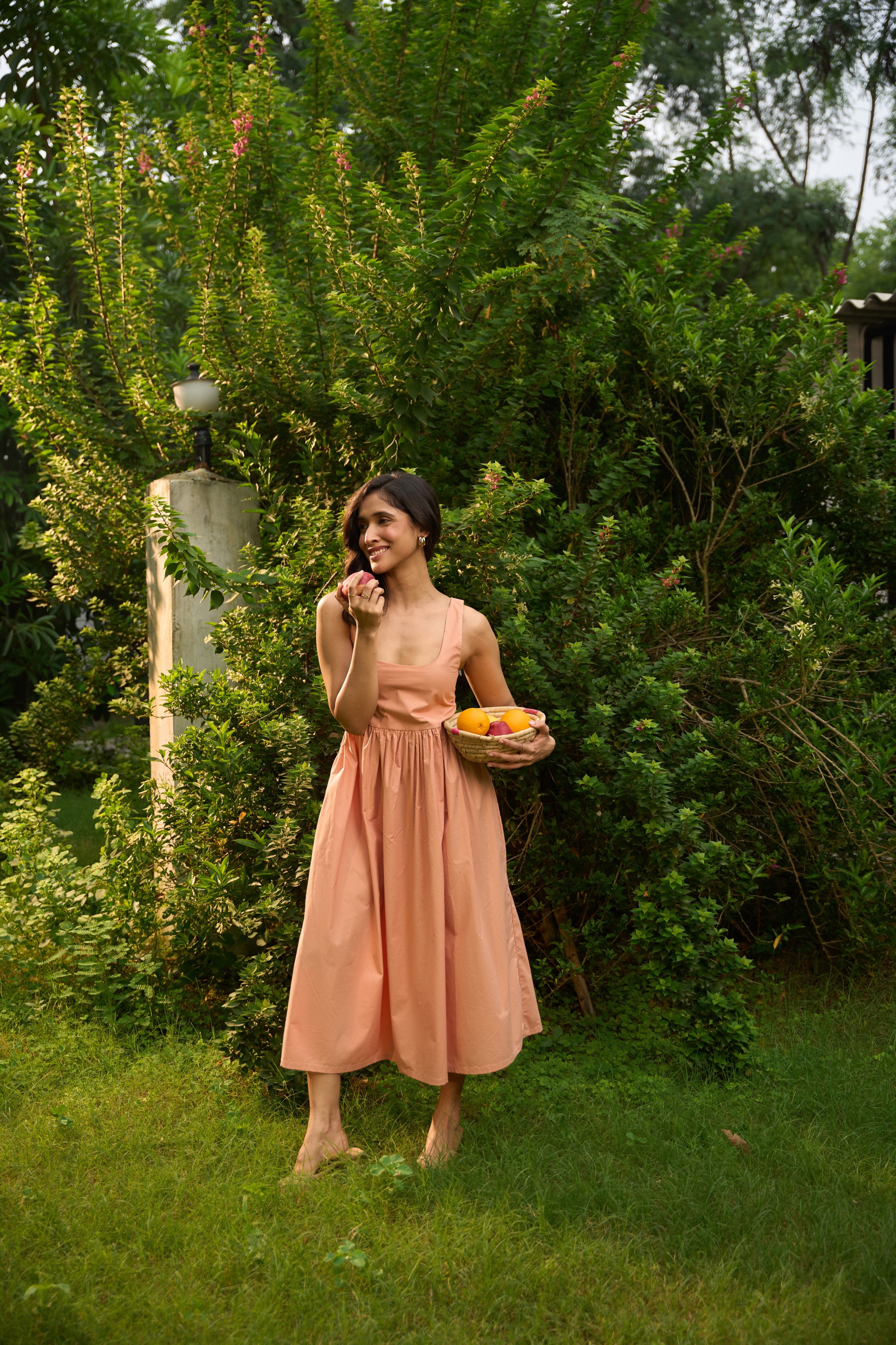 Woman in a peach dress holding a basket of fruit in a garden setting