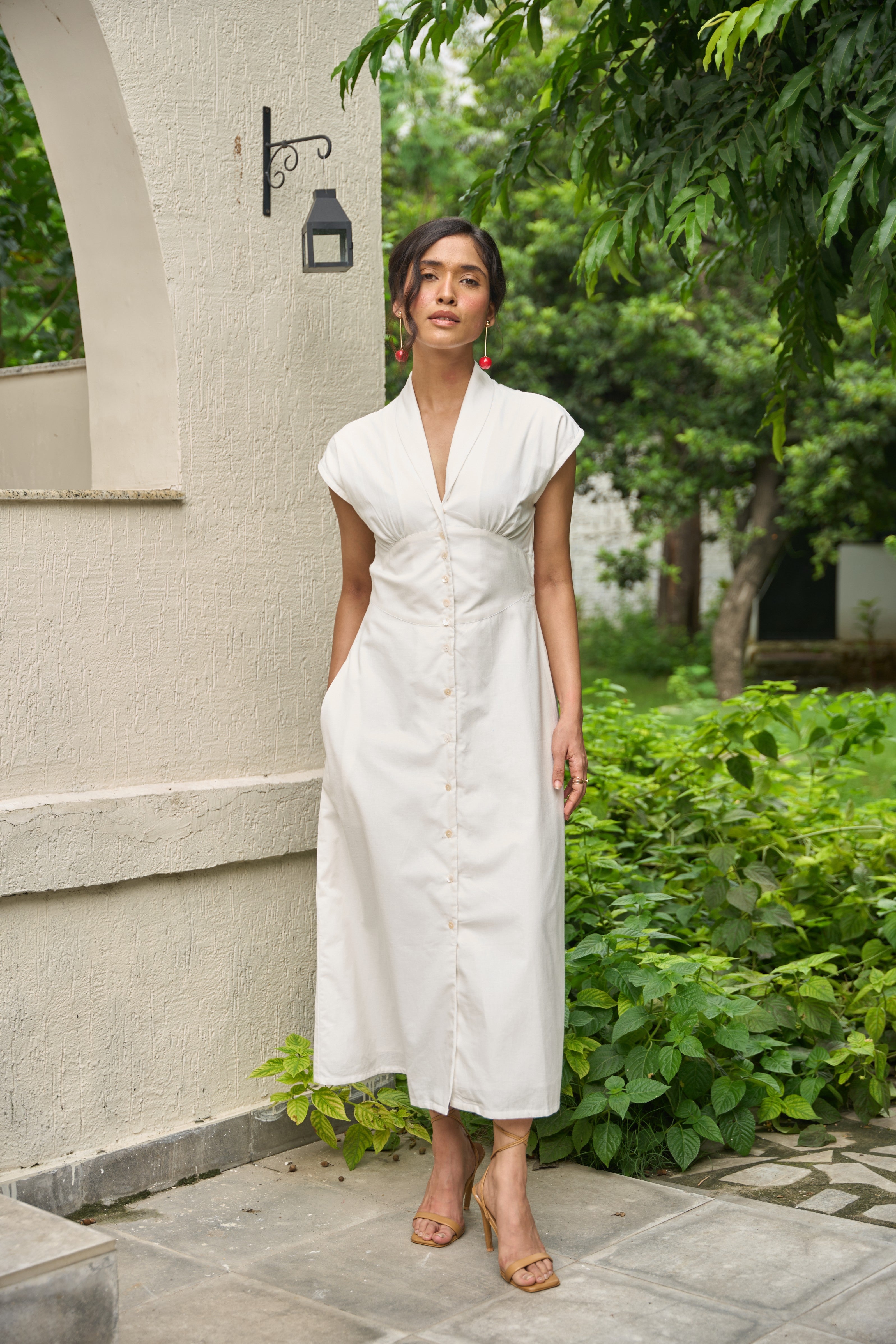 Woman in a white dress standing outdoors near a building with greenery.