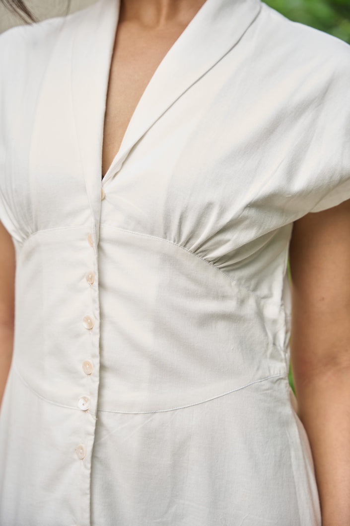 Close-up of a person wearing a light-colored dress with buttons.